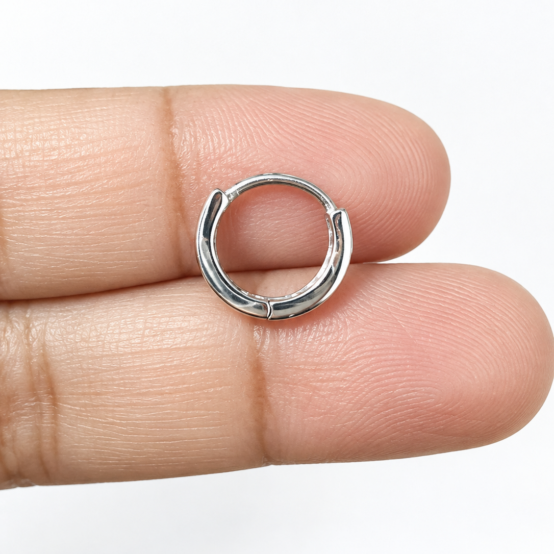 A small silver huggie hoop earring resting on a person's fingers against a plain white background.