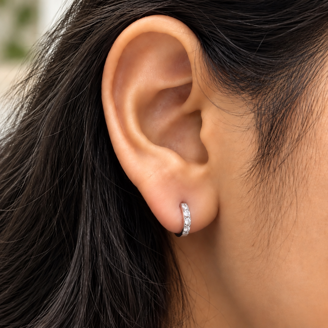 A close-up of a person's ear wearing a small 925 silver hoop earring set with clear stones.