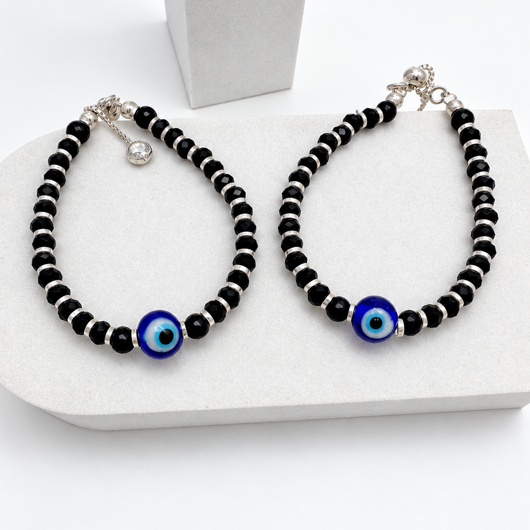'Silver Dolls' 925 sterling silver - two beaded nazariya bracelets displayed on a white jewelry stand. The bracelets are made of alternating black and silver beads, with a central blue and white evil eye charm.