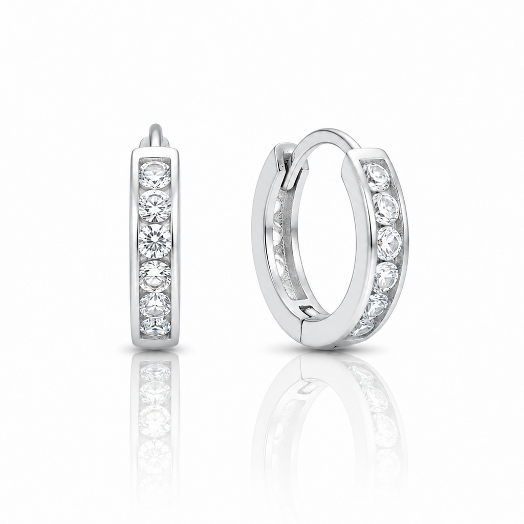 A pair of silver huggie hoop earrings with channel-set round clear gemstones, shown from the side and back on a reflective white surface.