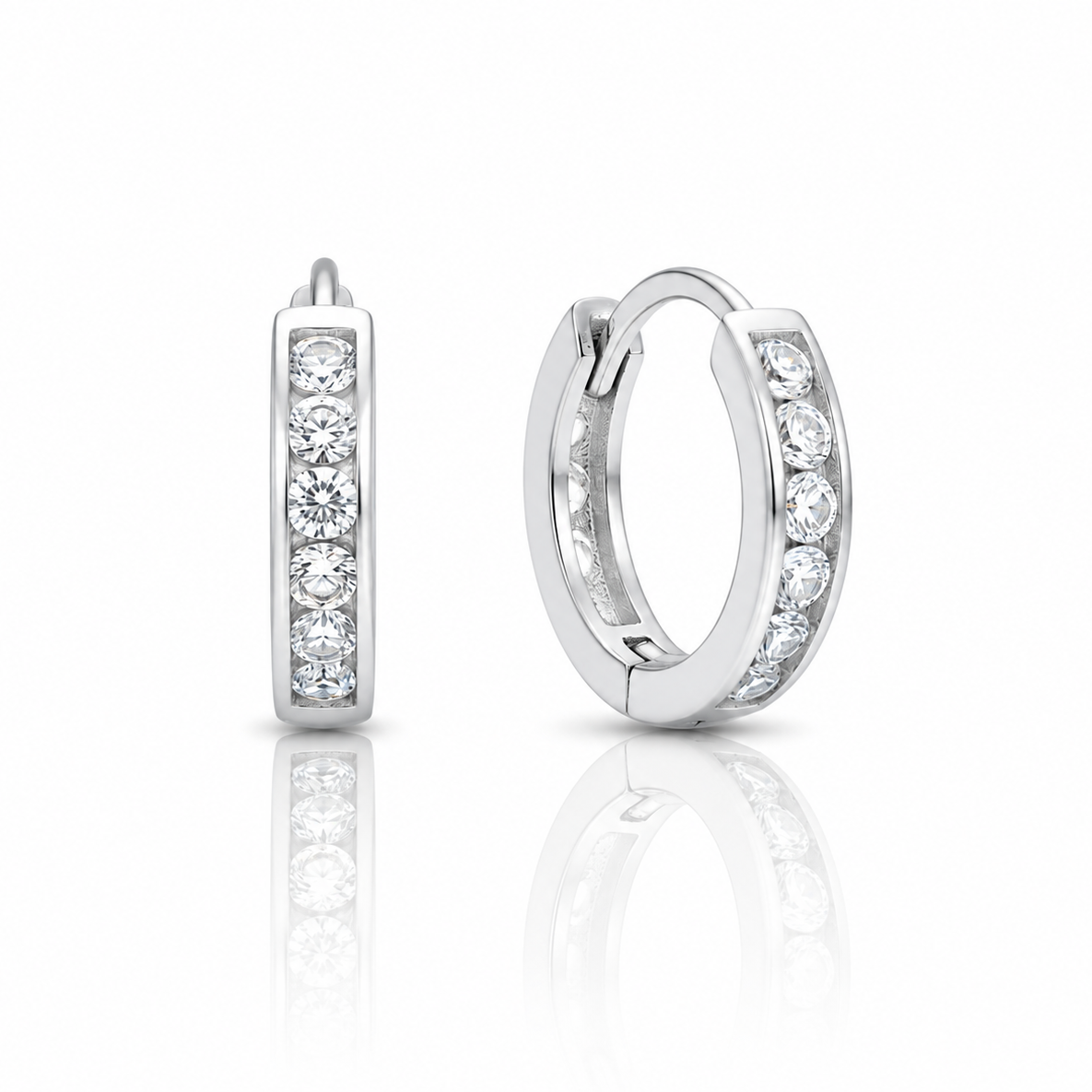A pair of silver huggie hoop earrings with channel-set round clear gemstones, shown from the side and back on a reflective white surface.